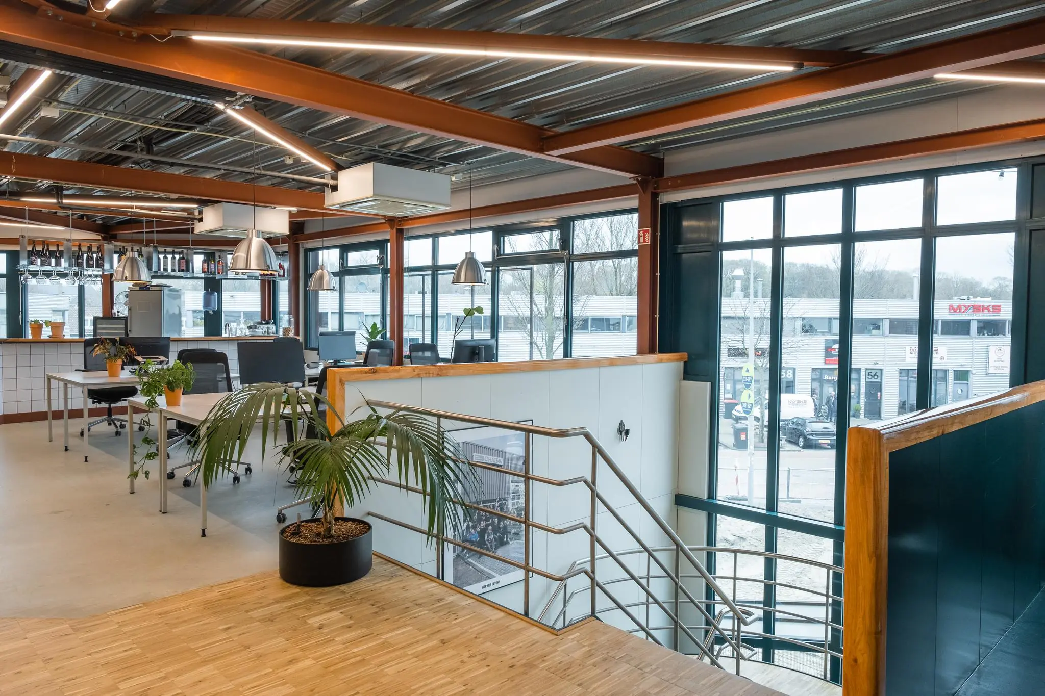 Modern ingericht kantoor met veel daglicht aan de Johan van Hasseltweg, met werkplekken, planten en een bar in industriële stijl.